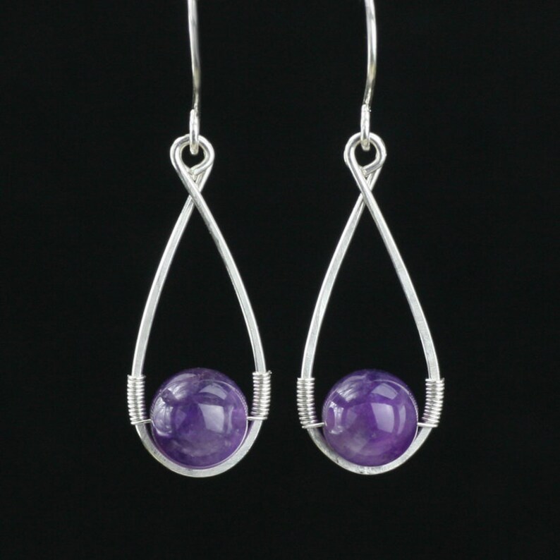 May include: A pair of silver dangle earrings with a purple amethyst gemstone in each. The earrings are made with a twisted wire design.