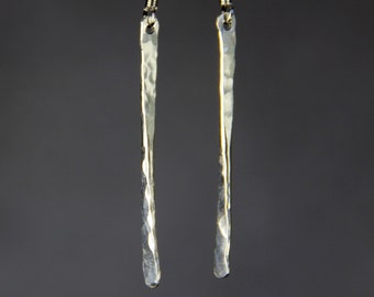 May include: A pair of silver dangle earrings with a hammered texture. The earrings are long and slender, with a simple hook closure.
