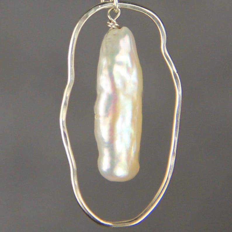 Pu&ograve; includere: Un orecchino d'argento con un anello ovale in filo metallico e una perla barocca bianca.
