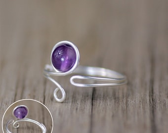 May include: A silver ring with a purple amethyst gemstone. The ring is made of wire and has a simple design.