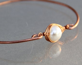 Op de afbeelding: Een delicate koperen draad armband met een enkele witte parel gewikkeld in koperdraad.