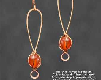 May include: A pair of gold dangle earrings with orange carnelian gemstone beads. The earrings are made with wire wrapped around the beads, creating a delicate and intricate design.