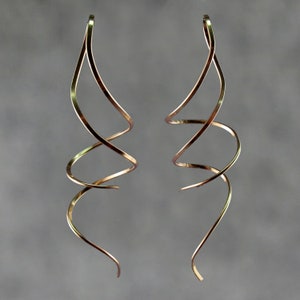 Può includere: Un paio di orecchini lunghi e a spirale color oro. Gli orecchini sono realizzati in filo sottile e ritorto.