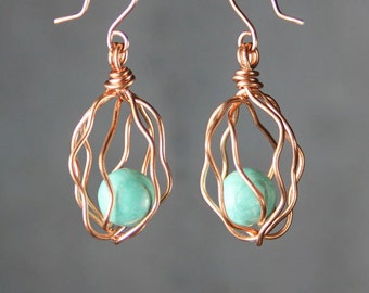 May include: A pair of copper wire earrings with a turquoise gemstone in each. The earrings are shaped like a cage with a round gemstone inside.