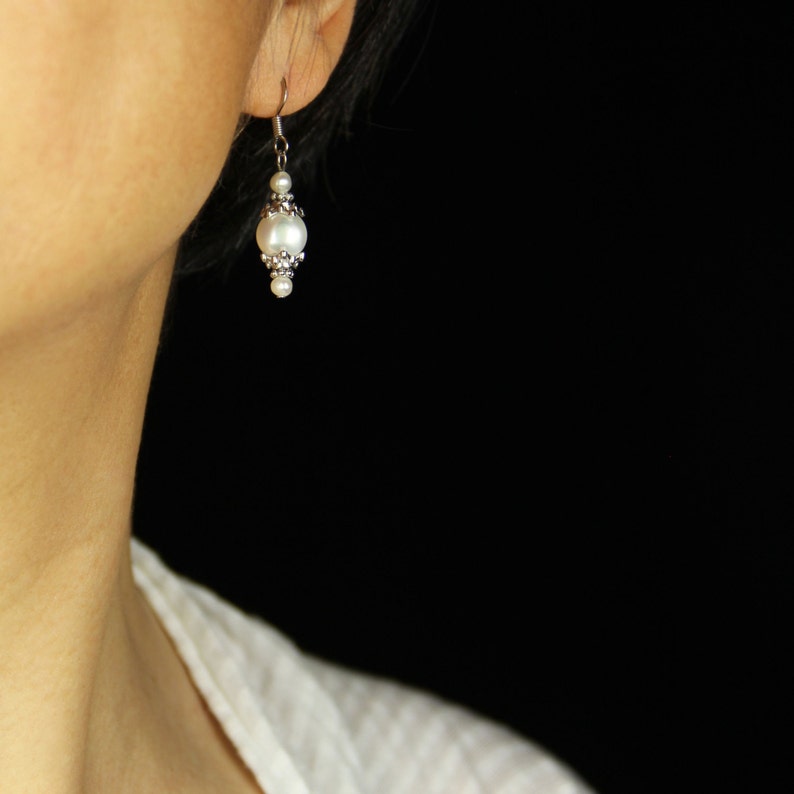 May include: A pair of silver earrings with a single white pearl on each earring.