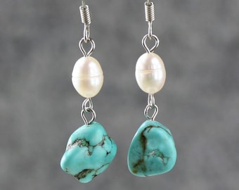 Op de afbeelding: Een paar oorhangers met turquoise stenen en witte parel accenten. De oorbellen zijn gemaakt van zilver en hebben een eenvoudig ontwerp.