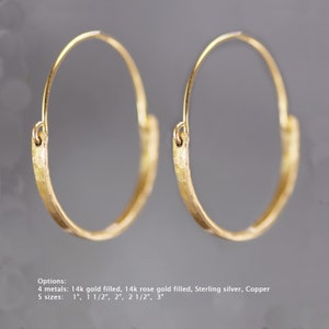 May include: A pair of gold hoop earrings with a hammered texture. The earrings are available in four metals: 14k gold filled, 14k rose gold filled, sterling silver, and copper. The earrings are available in five sizes: 1 inch, 1 1/2 inches, 2 inches, 2 1/2 inches, and 3 inches.