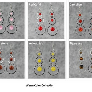 May include: A collection of six pairs of dangle earrings with silver hoops and gemstone beads. The earrings feature warm colors, including red coral, carnelian, gold sand stone, yellow jade, and tiger's eye. The earrings are labeled with their corresponding gemstone names. The text "Warm Color Collection" is displayed at the bottom of the image.