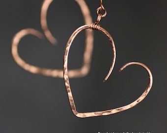 May include: A pair of copper heart-shaped earrings with a hammered texture. The earrings are open and have a simple wire design.