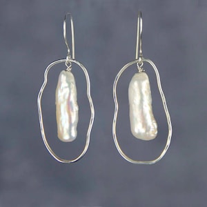 Pu&ograve; includere: Orecchini d'argento con una forma ovale irregolare unica e una singola perla barocca bianca appesa a ciascun orecchino.
