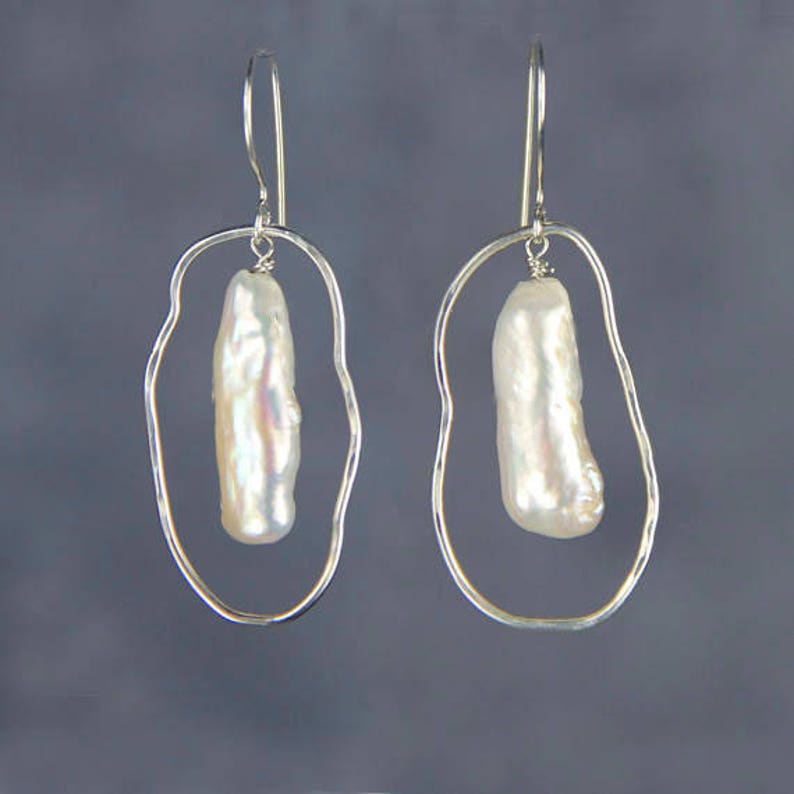 Pu&ograve; includere: Orecchini d'argento con una forma ovale irregolare unica e una singola perla barocca bianca appesa a ciascun orecchino.