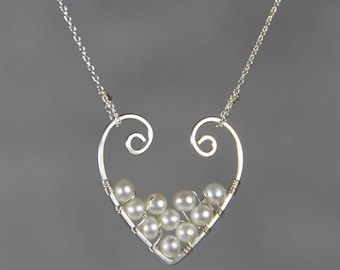 May include: A silver necklace with a heart-shaped pendant. The pendant is made of wire and has a cluster of white pearls in the center.