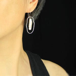 Pu&ograve; includere: Un orecchino d'argento con una perla bianca in una montatura ovale.