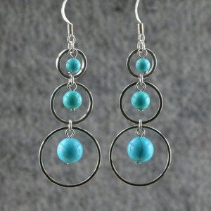 May include: Silver dangle earrings with turquoise stones and three circular hoops.