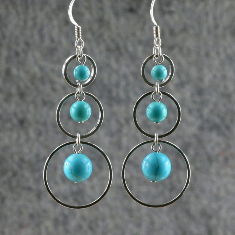 May include: Silver dangle earrings with turquoise stones and three circular hoops.