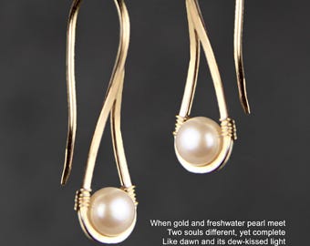 May include: A pair of gold-toned drop earrings featuring a single round white freshwater pearl at the base of each wire loop. The text on the image reads: When gold and freshwater pearl meet, Two souls different, yet complete, Like dawn and its dew-kissed light, Opposites drawn, our love is born.
