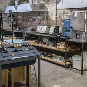 May include: A workshop with a variety of tools and equipment, including a metal workbench with tools, a metal shelving unit with various items, and a large metal oven with a digital display.