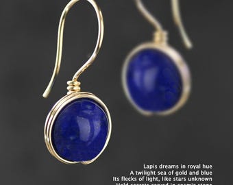 May include: Gold wire wrapped earrings with a round, deep blue lapis lazuli stone.  Lapis dreams in royal hue. A twilight sea of gold and blue. Its flecks of light, like stars unknown. Hold secrets carved in cosmic stone.
