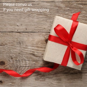 May include: A white gift box with a red ribbon tied in a bow. The box is sitting on a wooden surface. The text "Please convo us if you need gift wrapping" is visible above the box.