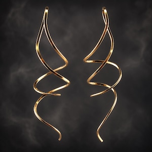 Op de afbeelding: Een paar lange, goudkleurige oorbellen bestaande uit een doorlopende, slanke metalen draad in de vorm van een langgerekte, open spiraal. De oorbellen hebben een glad, reflecterend oppervlak en een gebogen, vloeiend silhouet dat onderaan uitloopt.