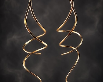 May include: A pair of long, gold-toned earrings featuring a continuous, slender metal wire shaped into an elongated, open spiral design. The earrings have a smooth, reflective surface and a curved, flowing silhouette that tapers to a point at the bottom.
