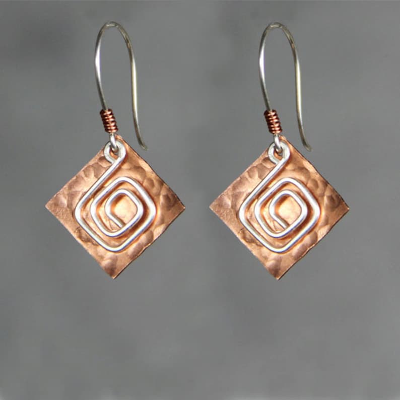 May include: A pair of copper earrings with a hammered finish and a silver wire spiral design.