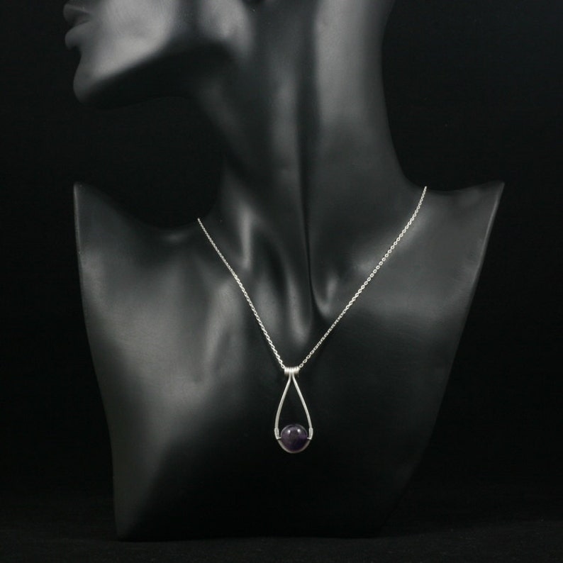May include: A silver chain necklace with a teardrop-shaped pendant featuring a round, purple amethyst gemstone.