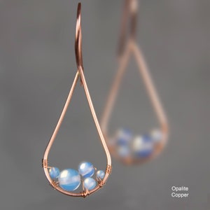 Pu&ograve; includere: Orecchini in filo di rame a forma di lacrima con un gruppo di pietre blu opalescenti.