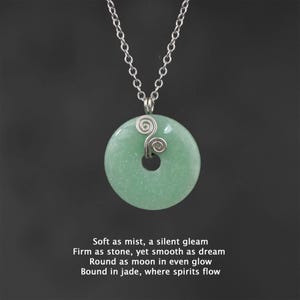 May include: A silver chain necklace with a round green jade pendant. The pendant has a silver wire design in the shape of two swirls.