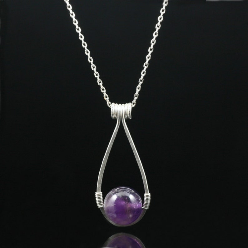 May include: A silver chain necklace with a teardrop-shaped pendant. The pendant holds a round, purple amethyst gemstone.
