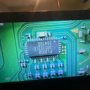 Puede incluir: Primer plano de una placa de circuito verde con un circuito integrado rectangular en el centro. El chip est&aacute; etiquetado como "P13USB 30532LE 20476G". La placa tiene varios componentes electr&oacute;nicos y trazas.