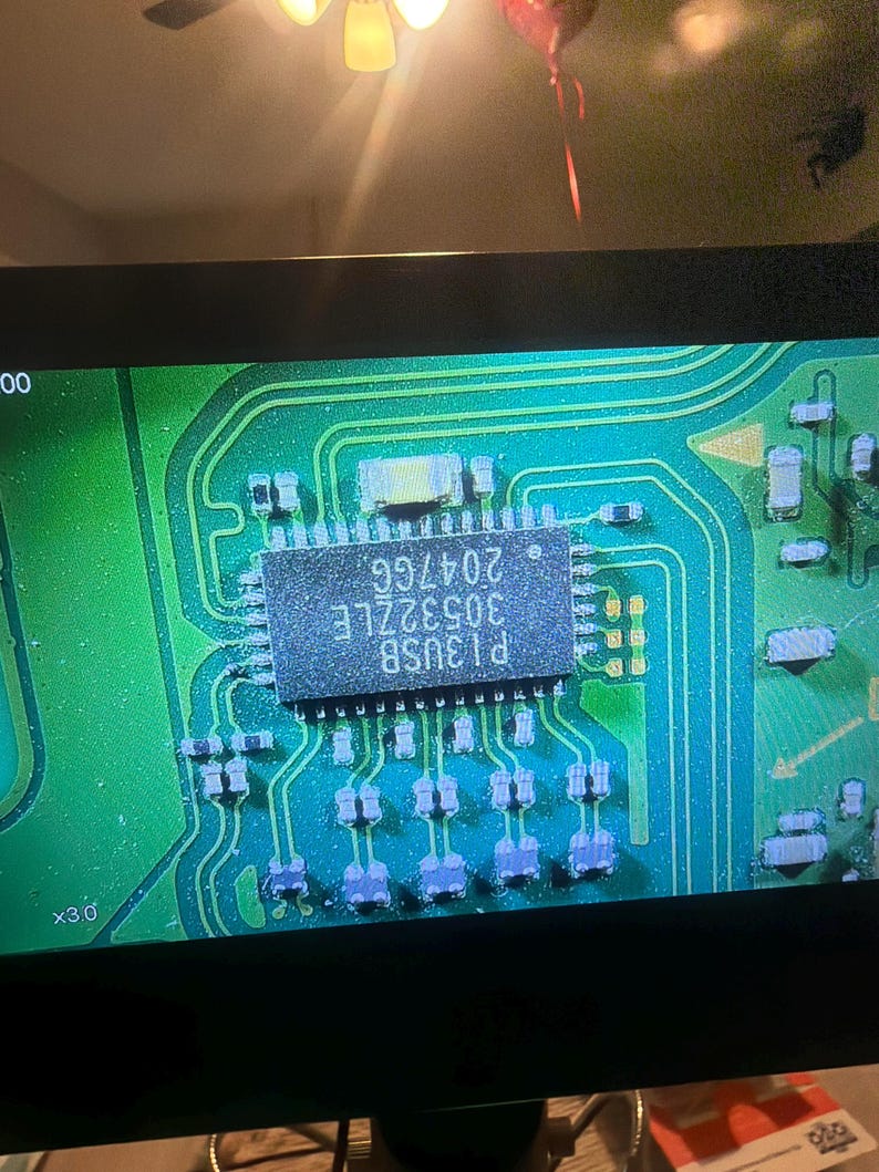 Puede incluir: Primer plano de una placa de circuito verde con un circuito integrado rectangular en el centro. El chip est&aacute; etiquetado como "P13USB 30532LE 20476G". La placa tiene varios componentes electr&oacute;nicos y trazas.