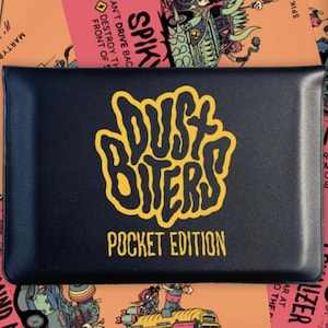 Op de afbeelding: Een zwarte kaartenhouder met gele tekst "Dust Biters Pocket Edition". De houder is omgeven door speelkaarten met illustraties van voertuigen en personages. Een cirkelvormig pictogram geeft aan dat het spel voor 2 spelers is.