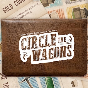 Può includere: Una scatola di gioco in pelle marrone con il titolo "CIRCLE THE WAGONS" in un font bianco e marrone. La scatola del gioco è circondata da carte di gioco con illustrazioni di revolver, edifici e altre immagini a tema western. Il gioco è per 2 giocatori.