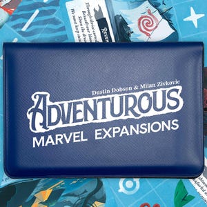 May include: A dark blue rectangular case with a textured surface featuring the white printed text ADVENTUROUS MARVEL EXPANSIONS and the names Dustin Dobson & Milan Zivkovic, positioned over a background of various illustrated game cards.