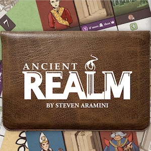 May include: A brown leather game box with the title "ANCIENT REALM" in white lettering. The game box is centered on a game board with various illustrated cards and game pieces. The text "BY STEVEN ARAMINI" is below the title. The game is for 1 player.