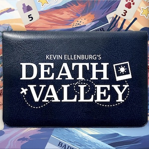 Puede incluir: Caja de juego de mesa azul oscuro con el título "DEATH VALLEY" en blanco. El juego es para 1-2 jugadores. La caja tiene una superficie texturizada. El fondo presenta cartas de juego con ilustraciones de paisajes desérticos.