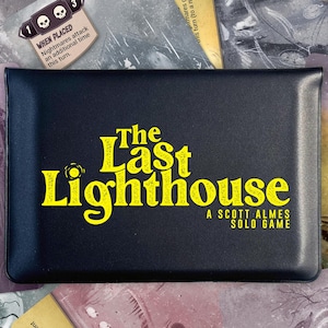 Może przedstawiać: Czarne pudełko z grą z żółtym napisem "The Last Lighthouse". Pudełko otoczone jest kartami do gry z ilustracjami latarni morskiej i innych elementów gry. Gra solo autorstwa Scotta Almesa.