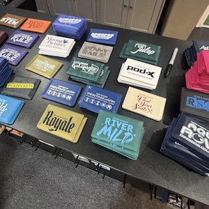 May include: A collection of various board game boxes and card decks, featuring titles like "Aqua Rove," "Wild Cats," and "Royale." The boxes are in various colors, including blue, green, and pink, with white text.