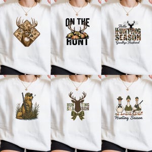 May include: A collection of six white crewneck sweatshirts, each featuring a unique hunting-themed graphic. Designs include a deer head in a camo diamond, text reading On The Hunt, Hello Hunting Season Goodbye Husband, a dog with a rifle, a deer with a camo bow tie, and three geese with hunting gear.