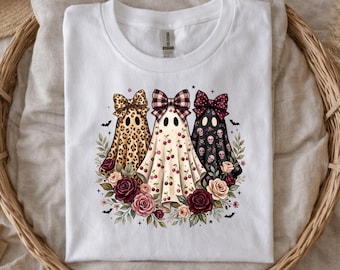 May include: A white short-sleeve t-shirt featuring a graphic of three ghosts wearing bows. The ghosts have leopard print, cherry, and skull patterns. The design includes a base of red and pink roses with green leaves and small black bats.