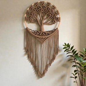 Può includere: Un arazzo da parete in macramè fatto a mano con un design ad albero. L'albero è realizzato con corda marrone ed è inserito in una cornice circolare in legno. Il design include un tronco, rami e foglie dettagliati, con lunghe frange.