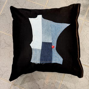 Puede incluir: Cojín cuadrado negro con un diseño de patchwork de mezclilla en forma del estado de Minnesota. Los parches de mezclilla son de varios tonos de azul. Un pequeño corazón rojo está cosido en la mezclilla. El cojín tiene un borde cosido marrón.