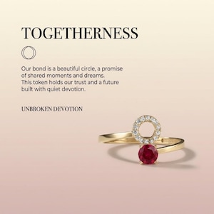 May include: A gold ring featuring a circular charm encrusted with small white stones and a single round red gemstone. The text TOGETHERNESS, UNBROKEN DEVOTION, and a paragraph about a bond and shared dreams are printed above the ring on a gradient background.