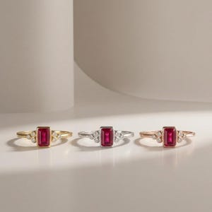 Peut inclure: Trois bagues pr&eacute;sentant une pierre rubis rouge centrale de taille baguette rectangulaire, flanqu&eacute;e de trois petits diamants blancs ronds de chaque c&ocirc;t&eacute;. Les bagues sont mont&eacute;es sur des anneaux en or jaune, m&eacute;tal argent&eacute; et or rose.