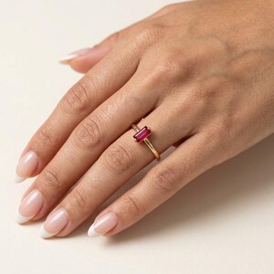 Puede incluir: Un anillo de oro con una sola piedra preciosa de rub&iacute; de corte baguette rectangular montada horizontalmente. La banda es delgada y pulida, mostrando un dise&ntilde;o sencillo que resalta el color rojo intenso de la piedra centrada.