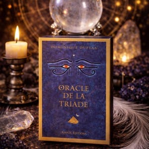 Puede incluir: Una caja de cartas de oráculo azul oscuro con ribete dorado y el título "Oracle de la Triade" en letras doradas. La caja presenta un diseño de ojo y el nombre del autor, Dominique Duplaa. Una vela encendida y una bola de cristal en el fondo.