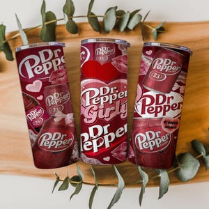以下が含まれることがあります： さまざまなデザインの、赤と白のDr. Pepperをテーマにしたタンブラー3つ。1つのタンブラーには、ハートと唇が付いた「Dr. Pepper Girly」と書かれています。他の2つのタンブラーには、Dr. Pepperのロゴとその他のグラフィックがあります。