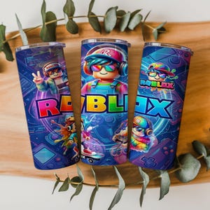 May include: Three cylindrical metal tumblers featuring a vibrant blue background with colorful Roblox-themed graphics. Each tumbler displays cartoon characters wearing headphones and sunglasses, along with the word Roblox in bold, multi-colored lettering.