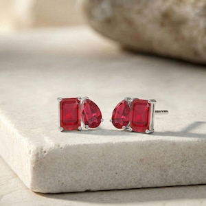 Puede incluir: Una taza de cerámica blanca con asa negra y el texto "But First, Coffee" en negrita negra. La taza se encuentra sobre un fondo borroso, sugiriendo un ambiente acogedor.